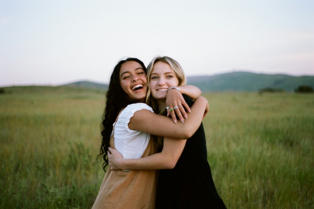 Two women hugging and laughing in a grassy field